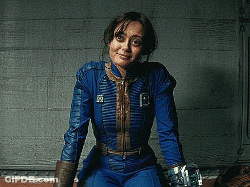 A Woman In A Blue Jumpsuit With A Vault Boy Emblem On The Front GIF