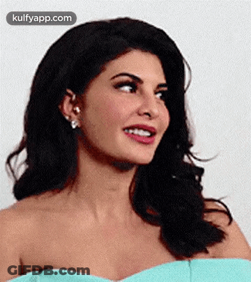 A Woman In A Blue Off The Shoulder Dress Is Smiling And Looking At The Camera . GIF