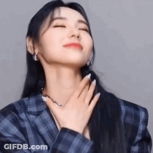 A Woman In A Blue Plaid Jacket Is Holding Her Hand To Her Chest . GIF