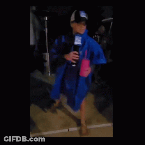 A Woman In A Blue Raincoat Holding A Microphone And A Pink Cup GIF