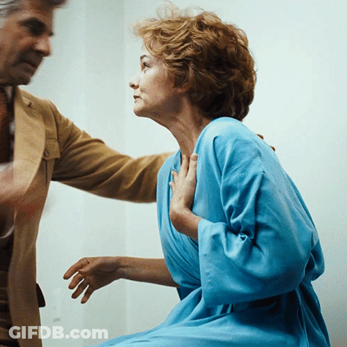 A Woman In A Blue Robe Is Being Held By A Man In A Tan Suit GIF