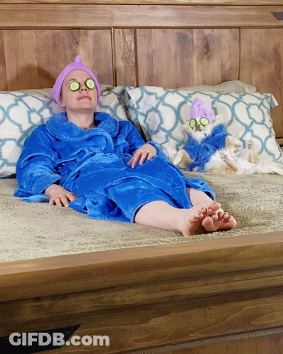 A Woman In A Blue Robe Is Laying On A Bed Next To A Small White Dog GIF