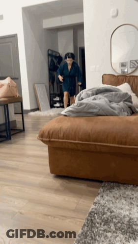 A Woman In A Blue Robe Is Standing In A Living Room GIF