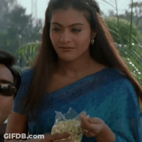 A Woman In A Blue Saree Is Holding A Bag Of Popcorn . GIF