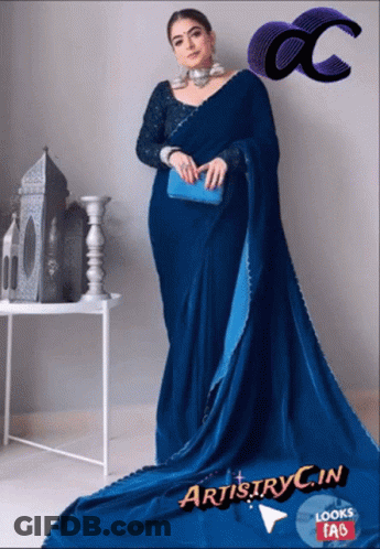 A Woman In A Blue Saree Is Standing In Front Of A White Table GIF