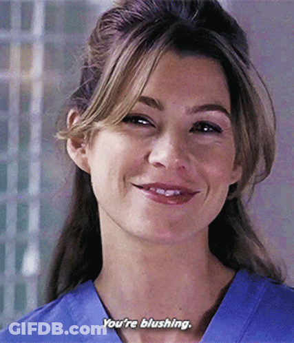 A Woman In A Blue Scrub Top Is Smiling And Saying You 'Re Blushing . GIF