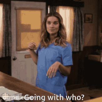 A Woman In A Blue Scrub Top Is Standing In Front Of A Door With The Words " Going With Who " Written Below Her GIF