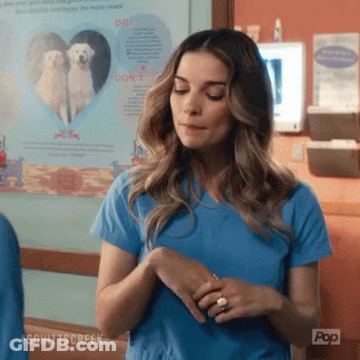 A Woman In A Blue Scrub Top Is Standing In Front Of A Poster Of A White Dog . GIF