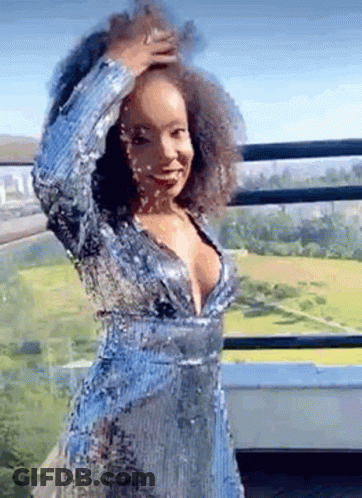 A Woman In A Blue Sequined Dress Is Standing On A Balcony Holding Her Hair . GIF