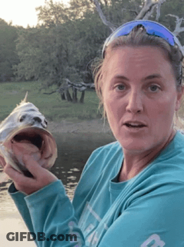 A Woman In A Blue Shirt Is Holding A Fish GIF