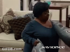 A Woman In A Blue Shirt Is Holding A Pillow In Front Of A Sign That Says " Savonce " GIF