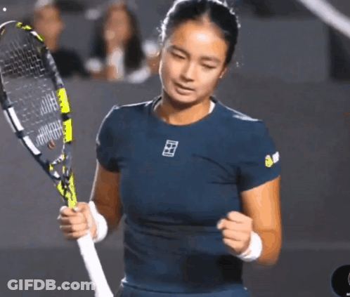 A Woman In A Blue Shirt Is Holding A Tennis Racquet In Her Hands GIF