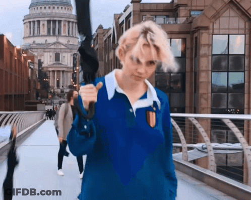 A Woman In A Blue Shirt Is Holding An Umbrella Over Her Shoulder GIF