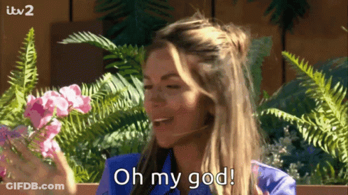 A Woman In A Blue Shirt Is Holding Flowers And Saying Oh My God GIF