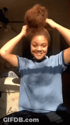 A Woman In A Blue Shirt Is Holding Her Hair Up In A Bun GIF