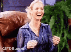A Woman In A Blue Shirt Is Laughing While Holding A Glass GIF