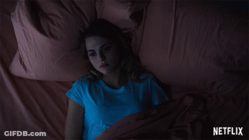 A Woman In A Blue Shirt Is Laying On A Bed With A Netflix Logo In The Corner GIF