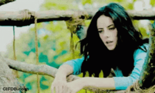 A Woman In A Blue Shirt Is Leaning On A Tree Branch GIF