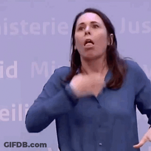 A Woman In A Blue Shirt Is Making A Funny Face In Front Of A Sign That Says Minister GIF