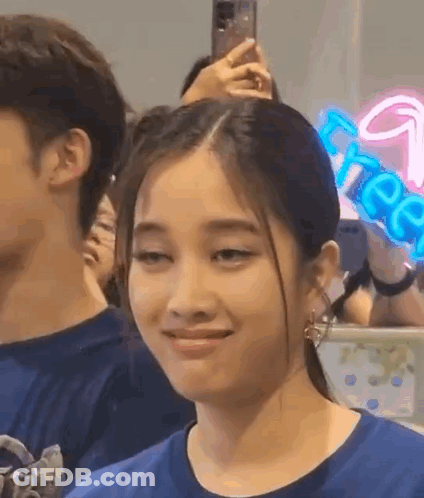 A Woman In A Blue Shirt Is Making A Funny Face While Sitting In A Crowd . GIF