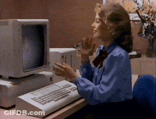 A Woman In A Blue Shirt Is Sitting At A Desk In Front Of An Old Computer . GIF