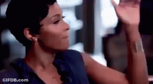 A Woman In A Blue Shirt Is Sitting At A Table With Her Hand Up . GIF