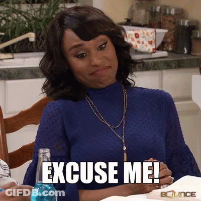 A Woman In A Blue Shirt Is Sitting At A Table With The Words Excuse Me On Her Face GIF