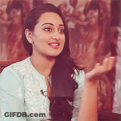 A Woman In A Blue Shirt Is Sitting In Front Of A Painting And Talking To Someone . GIF
