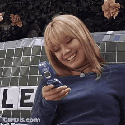 A Woman In A Blue Shirt Is Smiling While Holding A Blue Cell Phone GIF