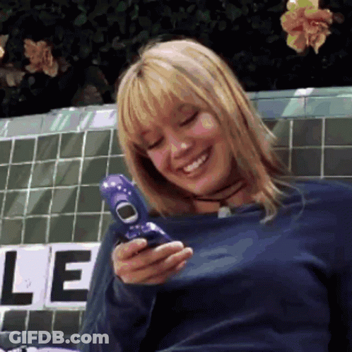 A Woman In A Blue Shirt Is Smiling While Holding A Purple Cell Phone GIF