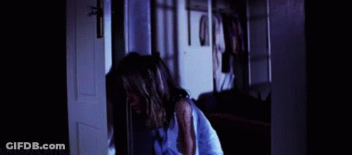A Woman In A Blue Shirt Is Standing In A Doorway With The Words " Undead Critic " On The Bottom Right GIF