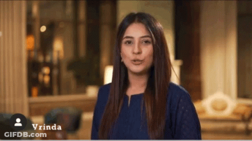 A Woman In A Blue Shirt Is Standing In A Living Room With The Name Vrinda On The Bottom GIF