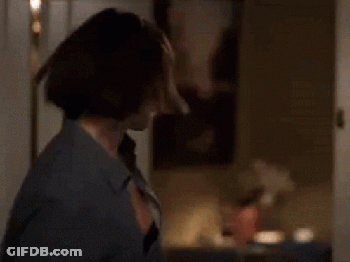 A Woman In A Blue Shirt Is Standing In A Room Holding A Bottle Of Wine . GIF