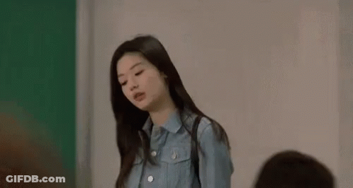 A Woman In A Blue Shirt Is Standing In Front Of A Green Wall . GIF