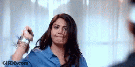 A Woman In A Blue Shirt Is Standing In Front Of A Mirror Holding Her Hair . GIF