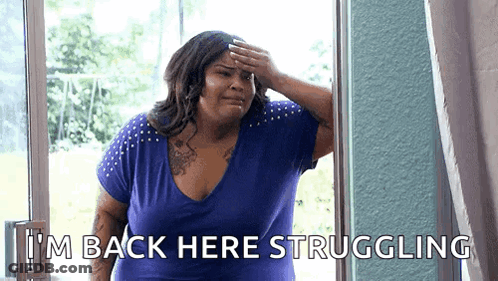 A Woman In A Blue Shirt Is Standing In Front Of A Window And Covering Her Forehead With Her Hand . GIF