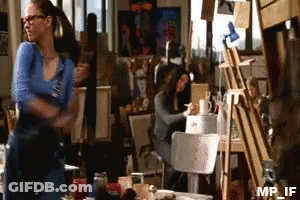 A Woman In A Blue Shirt Is Standing In Front Of An Easel With Mp_if Written On It GIF
