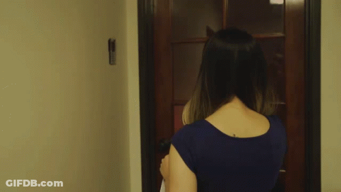 A Woman In A Blue Shirt Is Walking Through A Doorway GIF