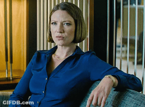 A Woman In A Blue Shirt Sits On A Grey Couch GIF