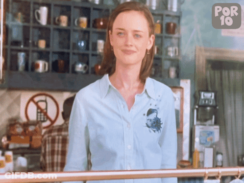 A Woman In A Blue Shirt Stands In Front Of A Sign That Says No Cell Phones GIF