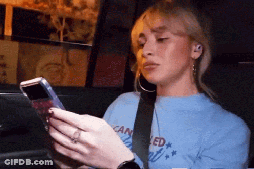 A Woman In A Blue Shirt That Says Canceled Is Looking At Her Phone GIF
