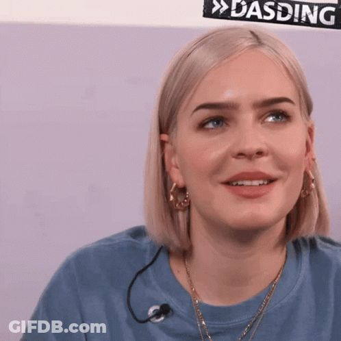 A Woman In A Blue Shirt With A Microphone Around Her Neck Is Smiling GIF