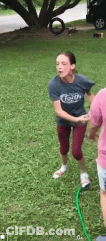 A Woman In A Blue Shirt With The Word Faith On It Is Jumping Over A Green Hose . GIF