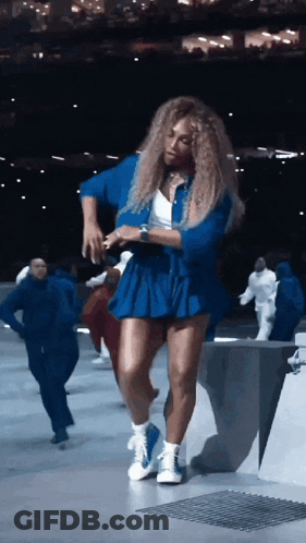A Woman In A Blue Skirt Is Dancing In A Dark Room GIF