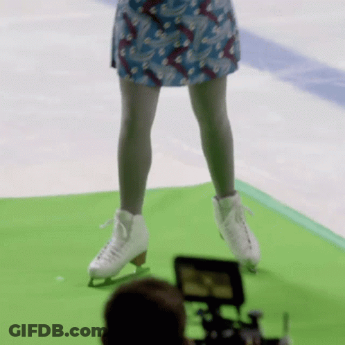 A Woman In A Blue Skirt Is Standing On A Green Mat Wearing Ice Skates GIF