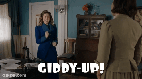 A Woman In A Blue Suit Is Standing Next To Another Woman In A Green Dress And The Words Giddy-Up Are Visible GIF