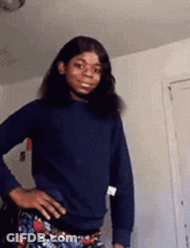 A Woman In A Blue Sweater And Floral Pants Is Standing With Her Hands On Her Hips . GIF
