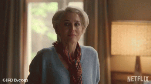 A Woman In A Blue Sweater And Scarf Stands In Front Of A Netflix Sign GIF