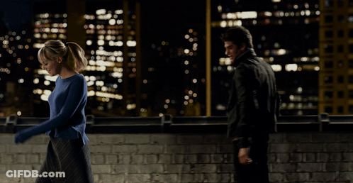 A Woman In A Blue Sweater Is Being Held By A Man In A Black Suit GIF
