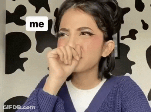 A Woman In A Blue Sweater Is Covering Her Mouth With Her Hand In Front Of A Cow Print Wall . GIF